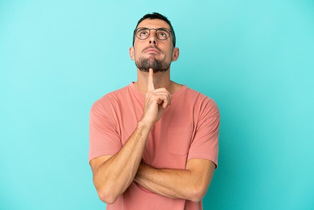 Foto joven apuesto hombre caucásico aislado sobre fondo azul con gafas y mirando hacia arriba