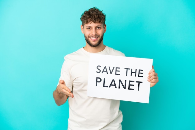 Joven apuesto hombre caucásico aislado sobre fondo azul sosteniendo un cartel con texto Save the Planet haciendo un trato