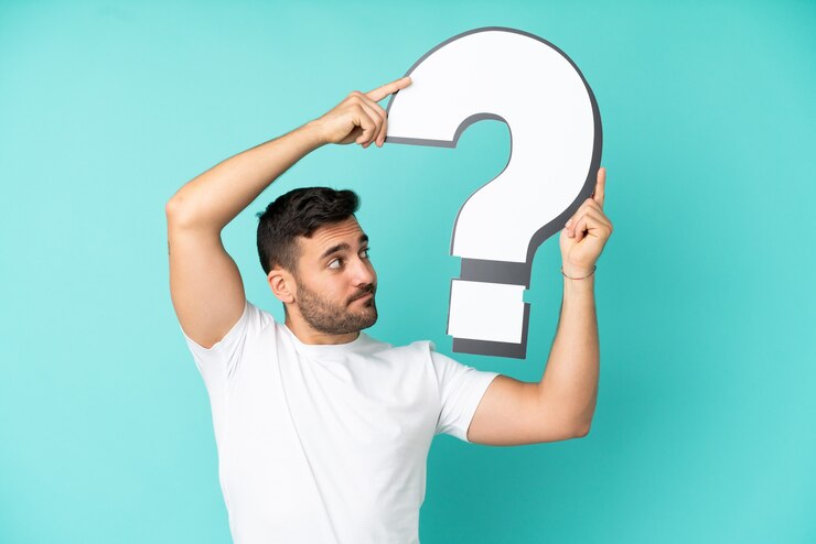 Foto joven apuesto hombre caucásico aislado sobre fondo azul sosteniendo un icono de signo de interrogación