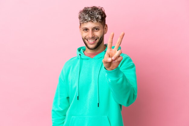 Joven apuesto hombre caucásico aislado sobre fondo rosa sonriendo y mostrando el signo de la victoria