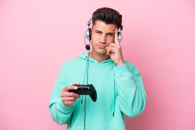 Joven apuesto hombre caucásico jugando con un controlador de videojuegos aislado en un fondo rosa pensando en una idea