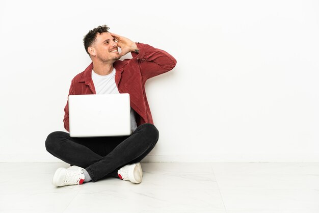 Joven apuesto hombre caucásico sentado en el suelo con una computadora portátil se ha dado cuenta de algo y tiene la intención de la solución