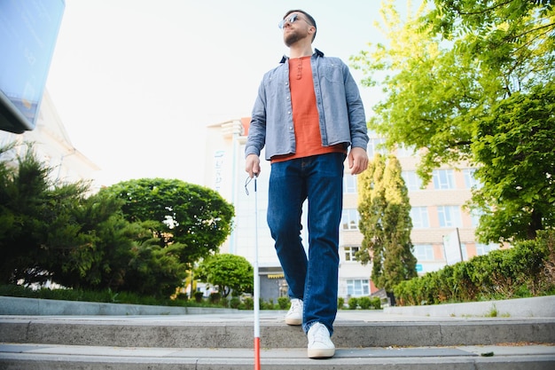 Joven apuesto hombre ciego caminando con bastón en la ciudad