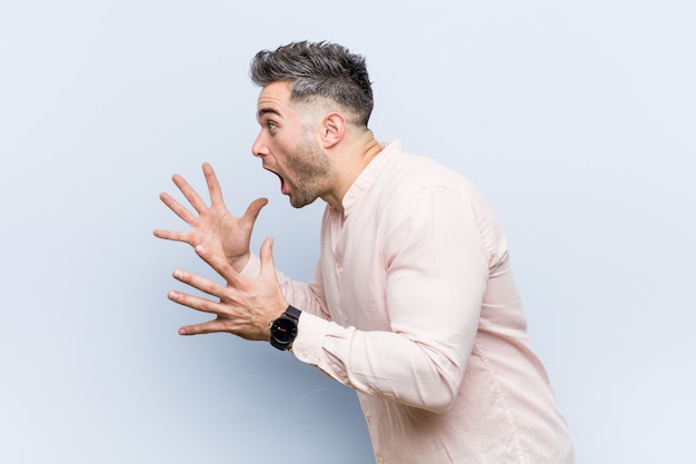 El joven apuesto hombre fresco grita fuerte, mantiene los ojos abiertos y las manos tensas.