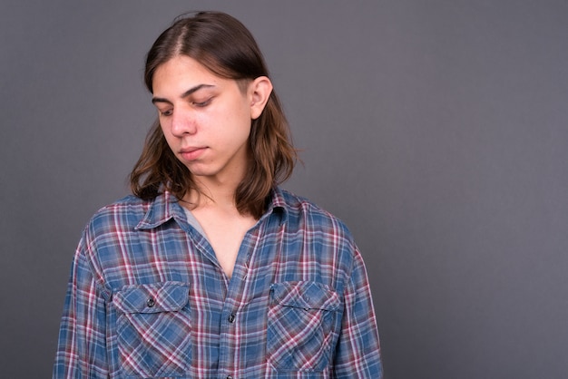 Joven apuesto hombre hipster andrógino con cabello largo contra la pared gris