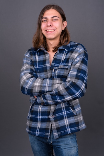 Joven apuesto hombre hipster andrógino con cabello largo contra la pared gris