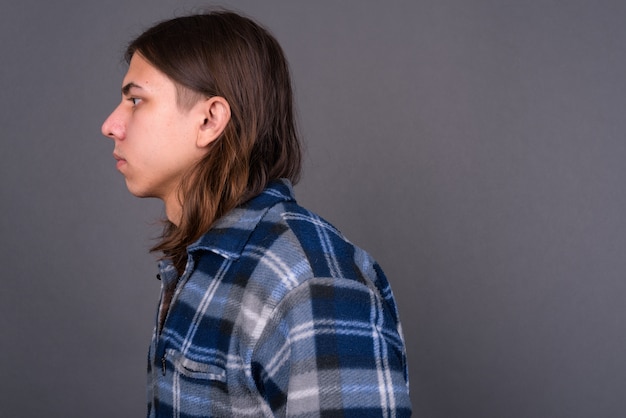 Foto joven apuesto hombre hipster andrógino con cabello largo contra la pared gris