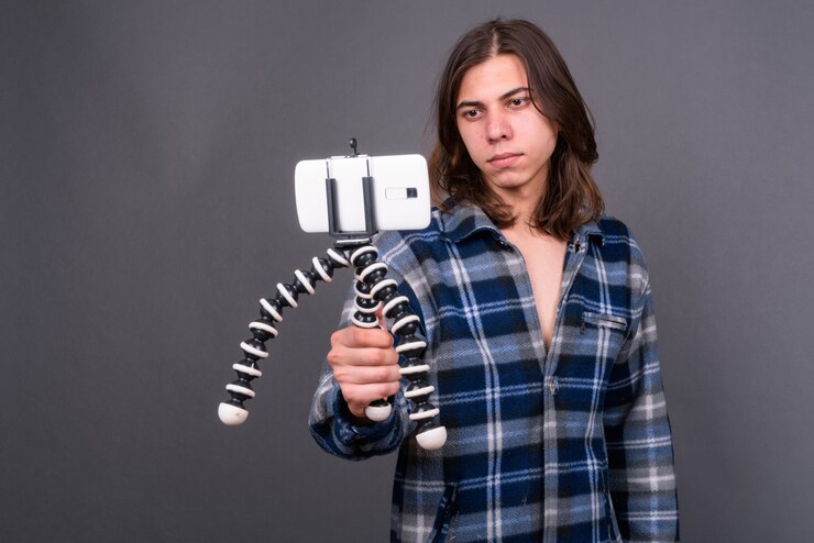 Foto joven apuesto hombre hipster andrógino con cabello largo contra la pared gris