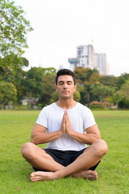 Joven apuesto hombre hispano meditando con las manos juntas en el parque