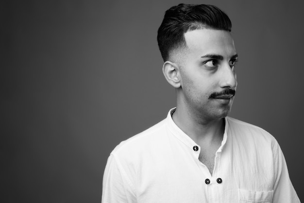 Joven apuesto hombre iraní con bigote vistiendo camisa blanca contra la pared gris en blanco y negro