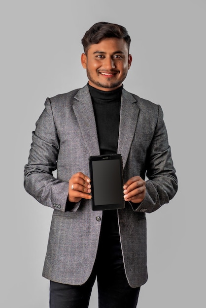 Joven apuesto hombre de negocios que muestra una pantalla en blanco de un teléfono inteligente o un teléfono móvil o una tableta con fondo gris