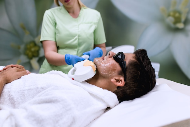 Joven apuesto hombre recibiendo procedimiento de cosmetología de depilación en la cara en la clínica de spa de belleza cosmética.