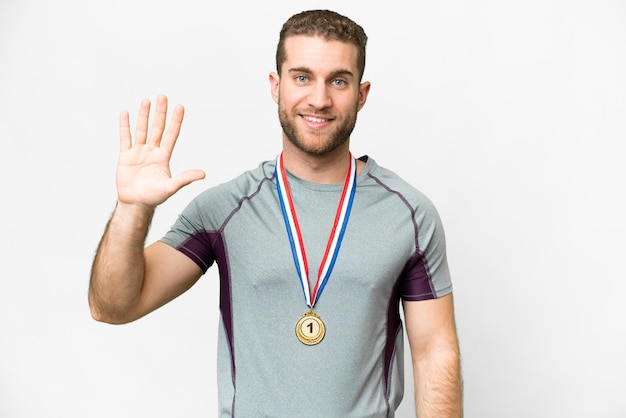 Joven apuesto hombre rubio con medallas sobre fondo blanco aislado contando cinco con los dedos