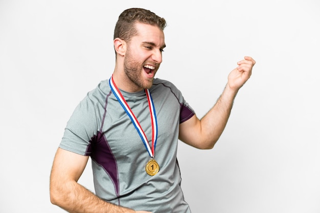 Joven apuesto hombre rubio con medallas sobre fondo blanco aislado haciendo gesto de guitarra