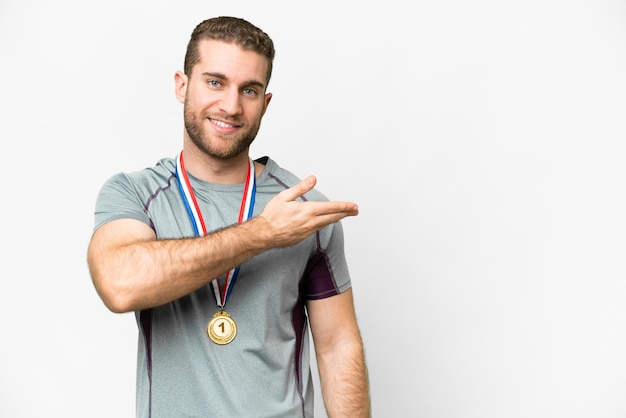 Joven apuesto hombre rubio con medallas sobre fondo blanco aislado que presenta una idea mientras mira sonriendo hacia