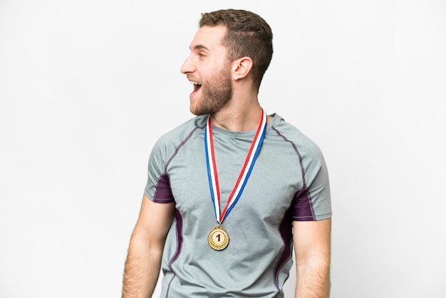 Joven apuesto hombre rubio con medallas sobre fondo blanco aislado riendo en posición lateral