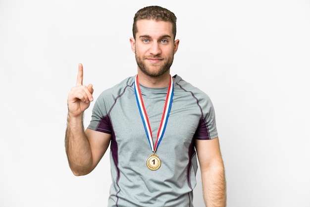 Joven apuesto hombre rubio con medallas sobre fondo blanco aislado señalando con el dedo índice una gran idea