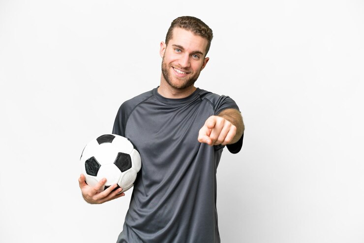 Foto joven apuesto hombre rubio sobre fondo blanco aislado con balón de fútbol y apuntando al frente