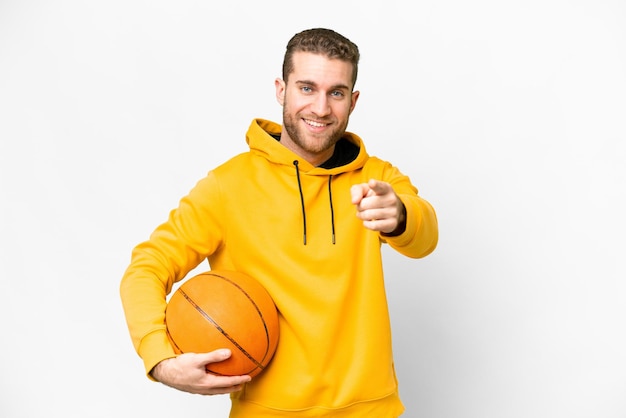 Joven apuesto hombre rubio sobre fondo blanco aislado jugando baloncesto y apuntando al frente