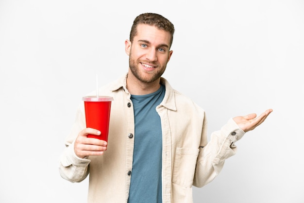 Joven apuesto hombre rubio sosteniendo soda sobre fondo blanco aislado extendiendo las manos a un lado para invitar a venir