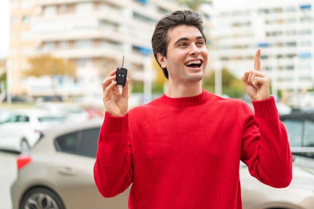 Joven apuesto con la llave del auto con la intención de darse cuenta de la solución mientras levanta un dedo