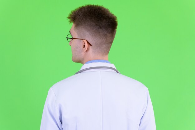 Joven apuesto médico con anteojos contra chroma key con pared verde