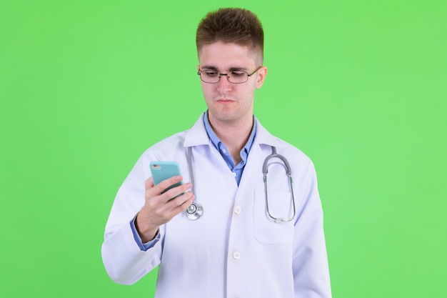 Joven apuesto médico con anteojos contra chroma key con pared verde