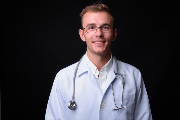 Joven apuesto médico con cabello rubio contra la pared negra