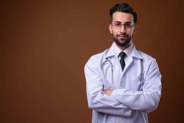 Joven apuesto médico iraní barbudo contra la pared marrón