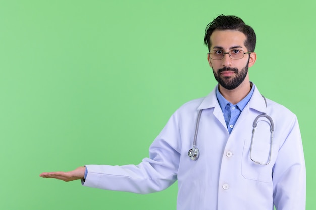 Joven apuesto médico persa barbudo contra la pared verde