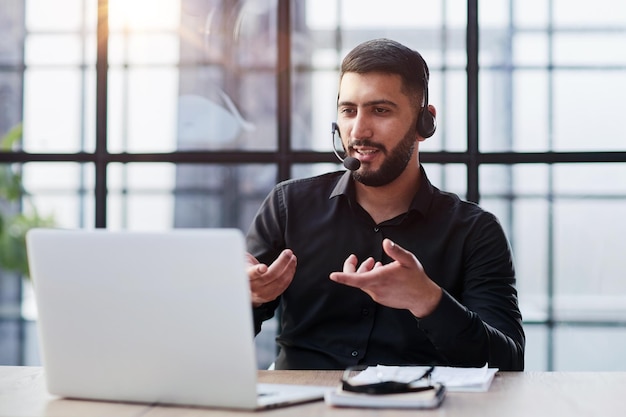 Joven apuesto operador telefónico de atención al cliente con auriculares trabajando en su oficina
