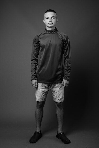 joven apuesto con el pelo corto con camisa de cuello alto contra la pared gris. en blanco y negro