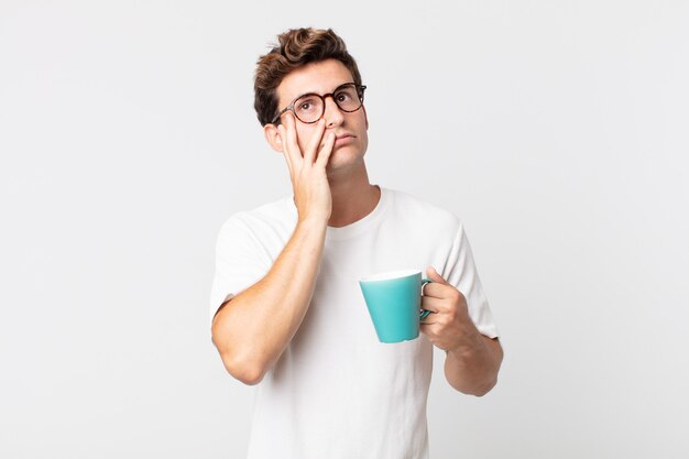 joven apuesto que se siente aburrido, frustrado y con sueño después de un cansado y sosteniendo una taza de café