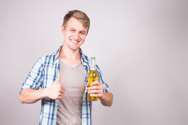 Un joven apuesto que se siente feliz mostrando los pulgares hacia arriba y sosteniendo una botella de cerveza.