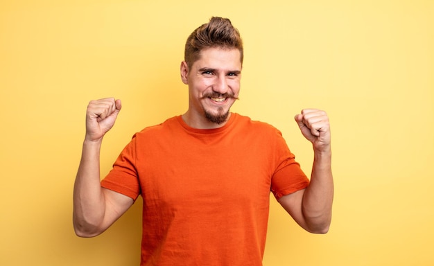 Joven apuesto que se siente feliz, sorprendido y orgulloso, gritando y celebrando el éxito con una gran sonrisa. extraño concepto de bigote