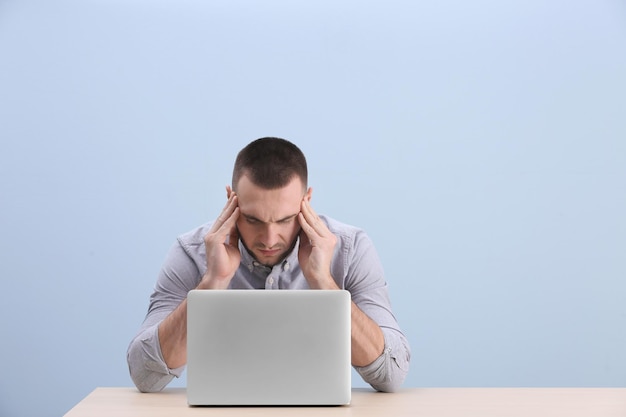 Un joven apuesto que sufre de dolor de cabeza mientras trabaja con una laptop con fondo de color