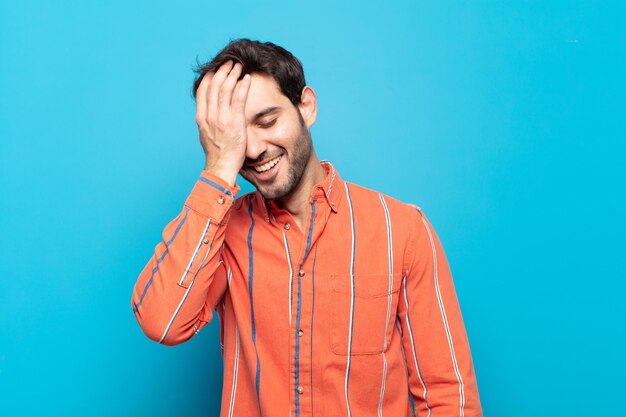 Joven apuesto riendo y dándose palmadas en la frente como diciendo dÃ ¢ Â € Â ™ ¡oh! Lo olvidé o fue un error estúpido