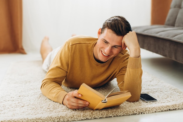 Un joven apuesto con ropa informal amarilla sentado en casa leyendo un libro