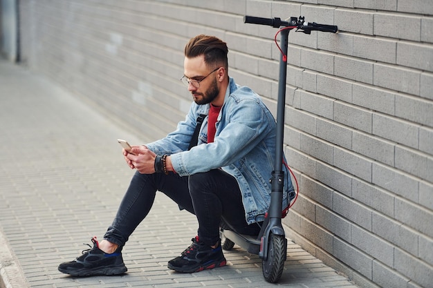 Un joven apuesto con ropa informal sentado en un scooter eléctrico al aire libre durante el día soleado