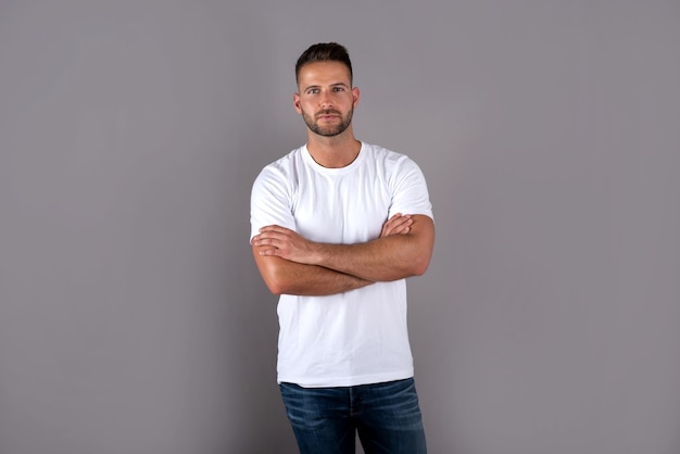 Foto un joven apuesto serio en una camiseta blanca de pie en gris