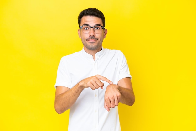 Joven apuesto sobre un aislado fondo amarillo haciendo el gesto de llegar tarde