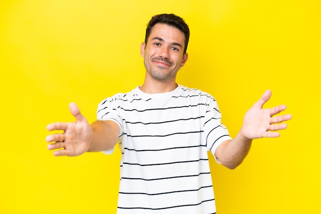 Joven apuesto sobre un fondo amarillo aislado que presenta e invita a venir con la mano