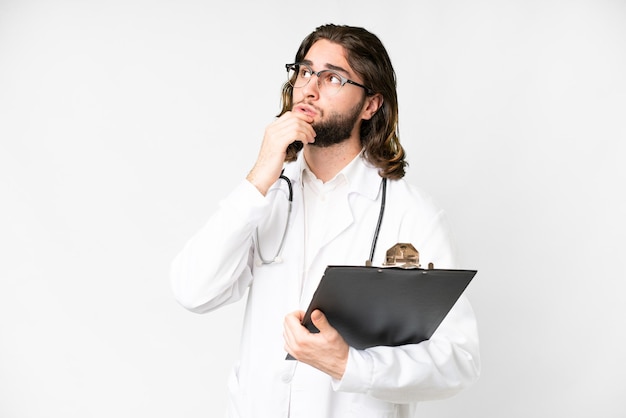 Un joven apuesto sobre un fondo blanco aislado con una bata de médico y sosteniendo una carpeta