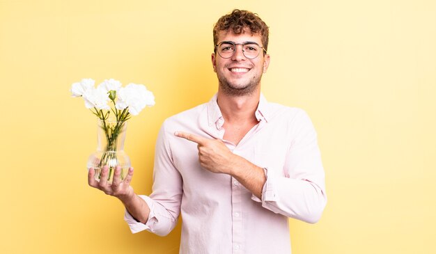 joven apuesto sonriendo alegremente, sintiéndose feliz y apuntando hacia un lado. concepto de flores