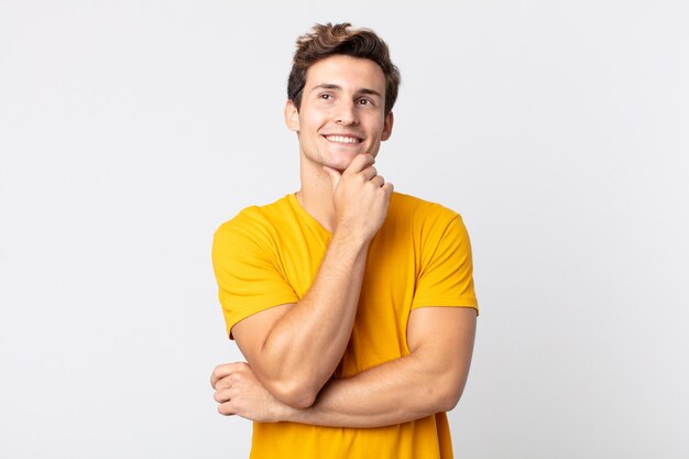 joven apuesto sonriendo alegremente y soñando despierto o dudando, mirando hacia un lado