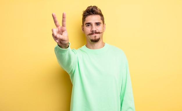 joven apuesto sonriendo y luciendo amigable, mostrando el número dos o segundo con la mano hacia adelante, contando hacia atrás. extraño concepto de bigote