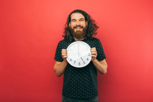 Foto un joven apuesto sostiene un reloj blanco redondo mientras sonríe a la cámara