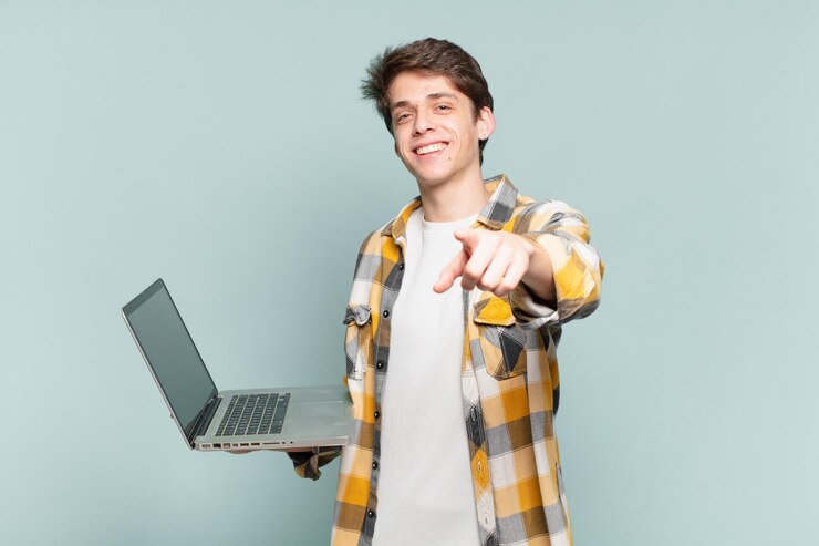Foto joven apuntando a la cámara con una sonrisa satisfecha, confiada y amistosa, eligiéndote a ti. concepto de computadora portátil