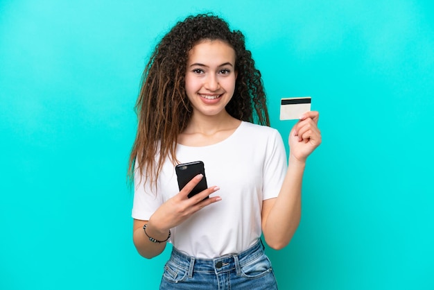 Foto joven árabe aislada de fondo azul comprando con el móvil con tarjeta de crédito