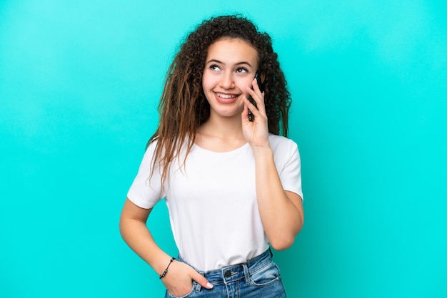 Joven árabe aislada de fondo azul manteniendo una conversación con alguien por teléfono móvil